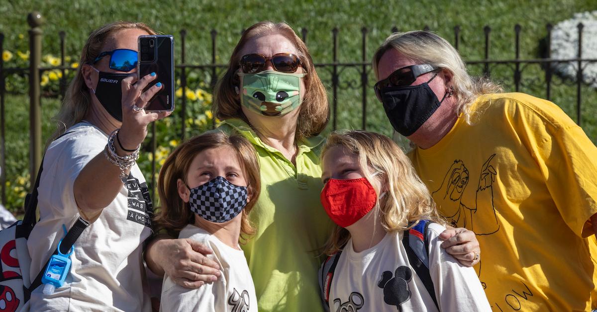 tre maskerade vuxna med solglasögon och två maskerade barn poserar för en selfie på disneyland