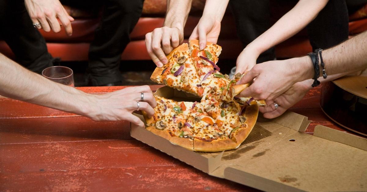 flere hænder rækker ud efter en skive pizza fra æsken ved samme itme