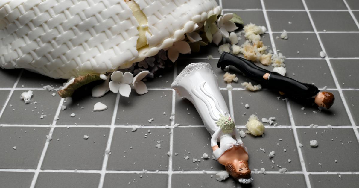 Estatuetas de noiva e noivo deitado perto de bolo de casamento destruído no chão de ladrilhos.