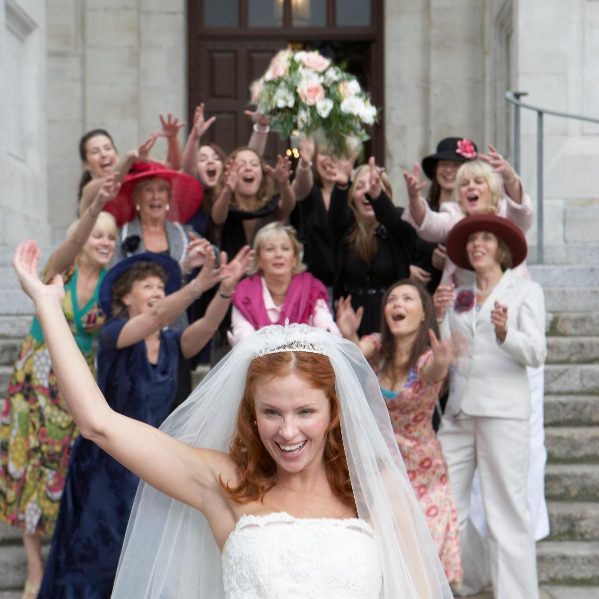 結婚式後、後ろにいる女性たちにブーケを投げる花嫁