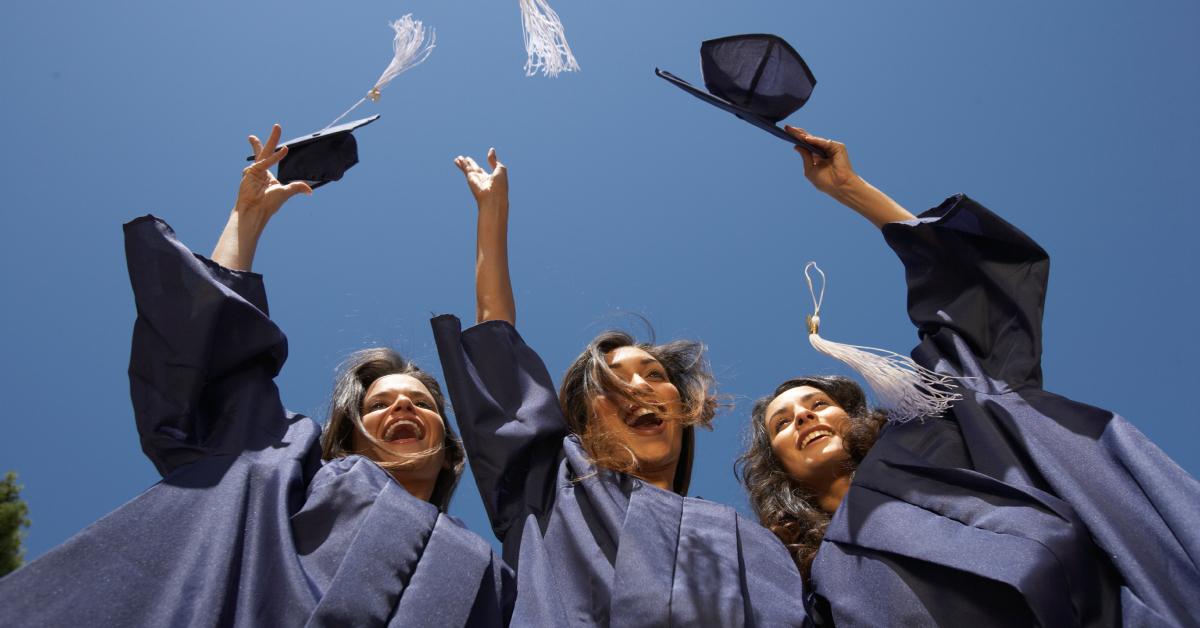 三名女大学毕业生将她们的帽子抛向空中。