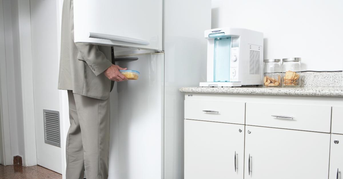사무실 부엌, 낮은 섹션에 있는 냉장고에서 음식을 제거하는 남자 - 스톡 사진