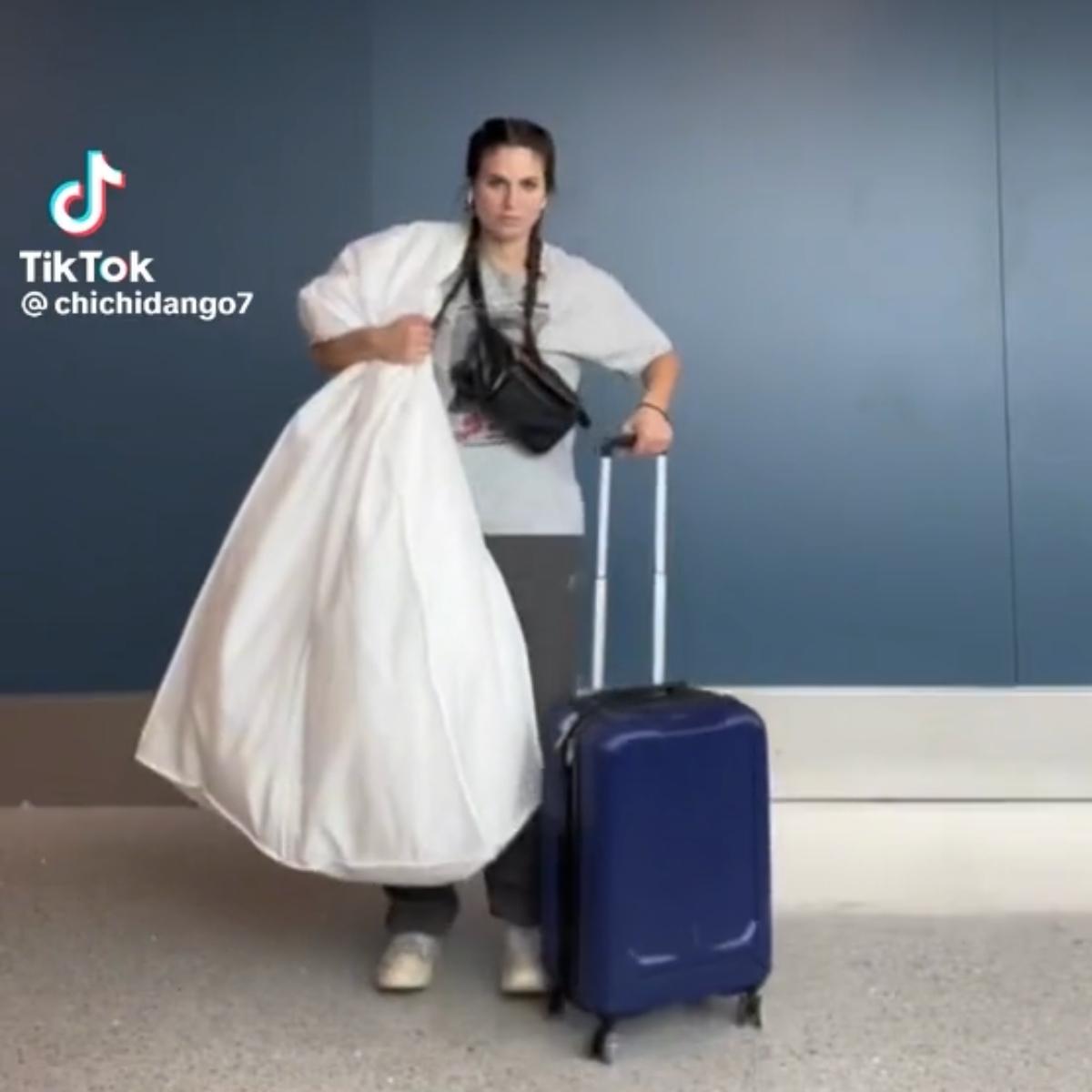 @chichidango7 attraversa l'aeroporto con un abito da sposa e una valigia.