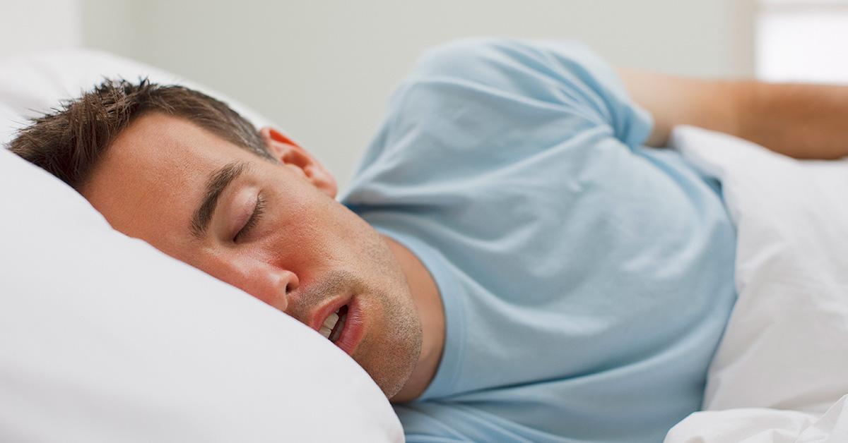 Mand sover med åben mund i en seng. 
