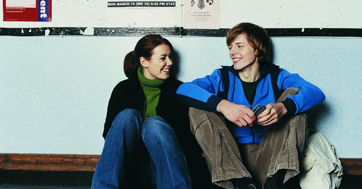 studenti universitari maschi e femmine seduti in un corridoio che si sorridono a vicenda