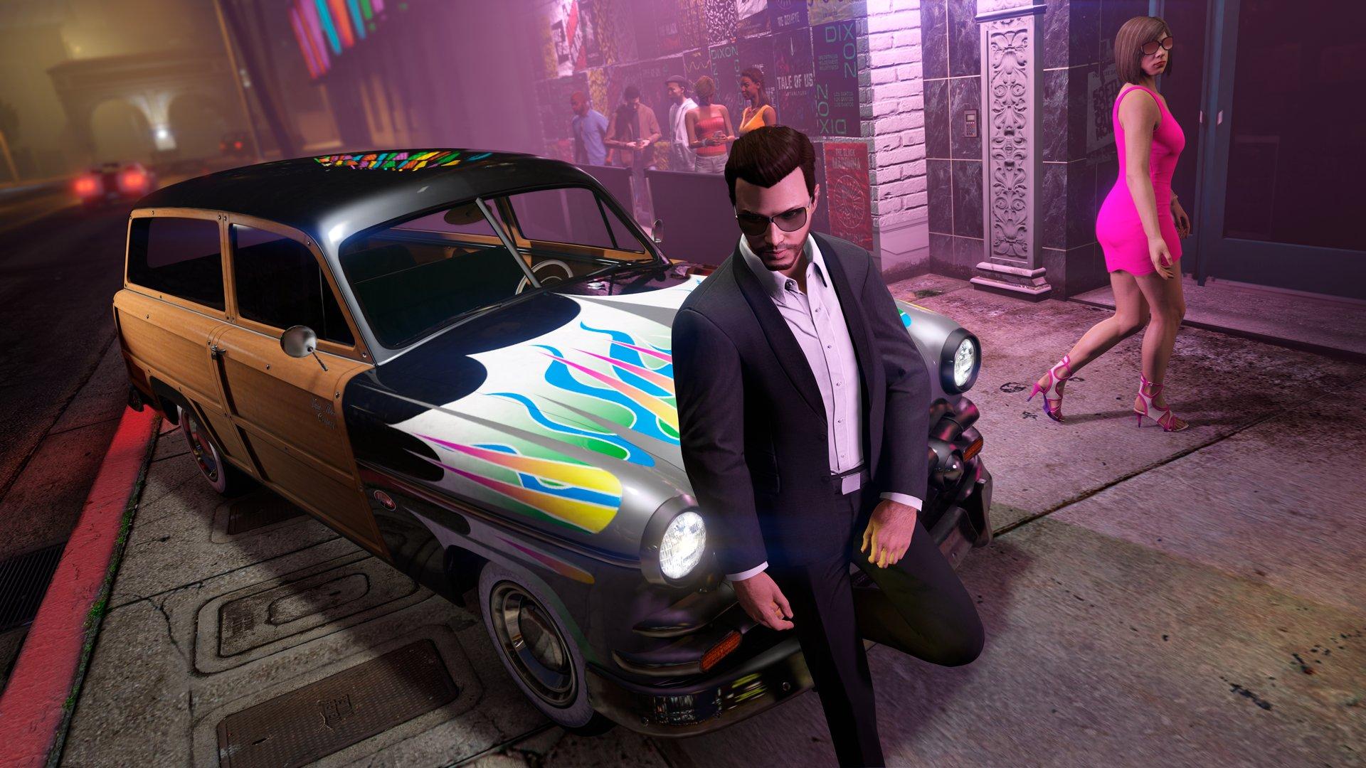 'GTA 온라인'에서 무지개 불꽃이 타오르는 차에 기대어 있는 남자와 핑크색 드레스와 하이힐을 신은 여자가 지나가고 있습니다.