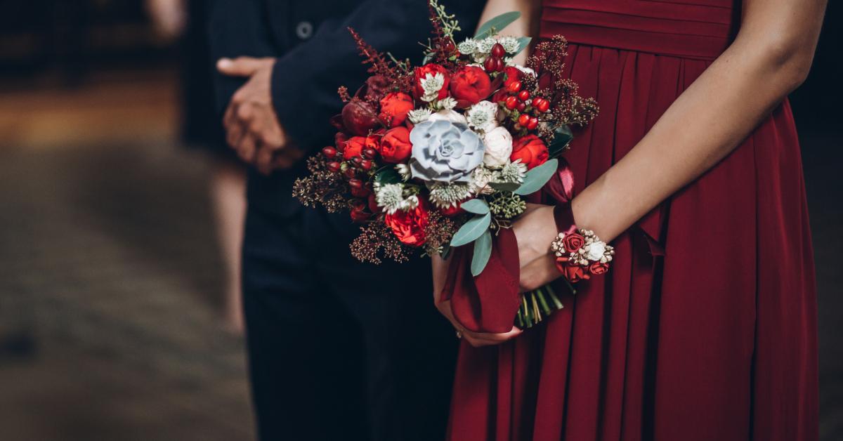 Eine Brautjungfer trägt ein rotes Kleid und hält einen rustikalen Blumenstrauß in der Hand.