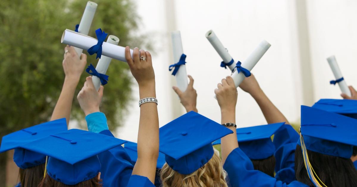 akademiker i kepsar och klänningar håller upp sina diplom