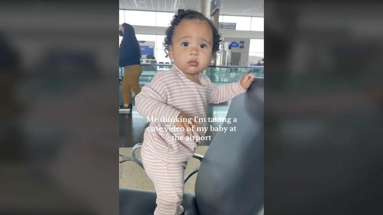 Das Baby steht auf einem Stuhl am Flughafen und schaut seine Mutter an