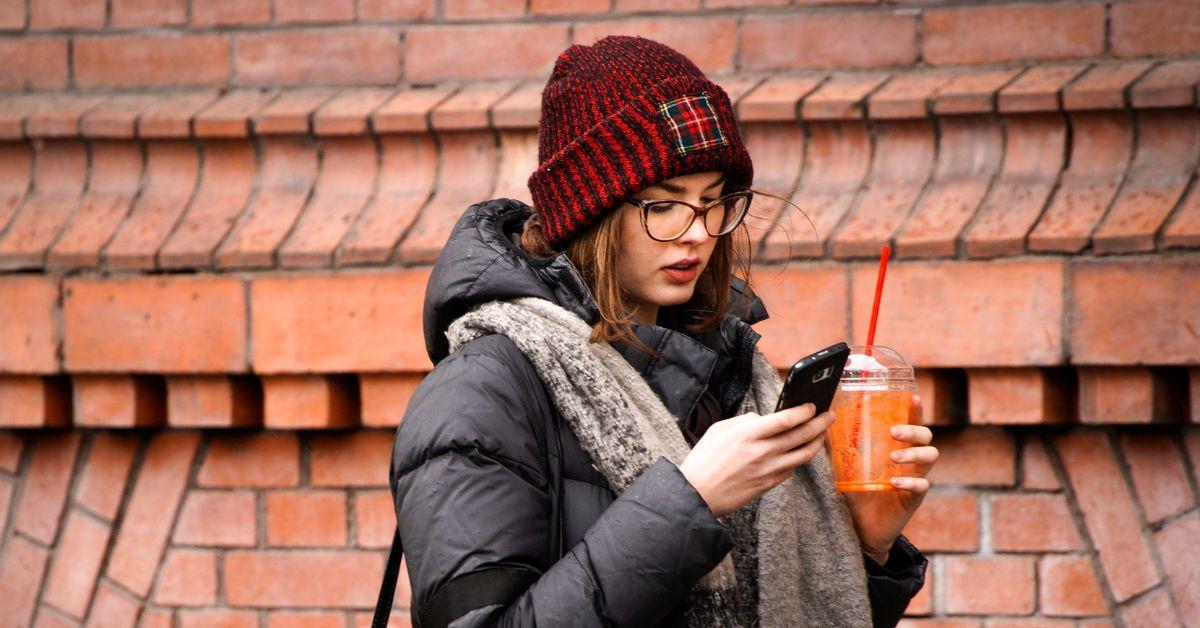 En kvinna som läser sin telefon medan hon håller en drink i sin andra hand