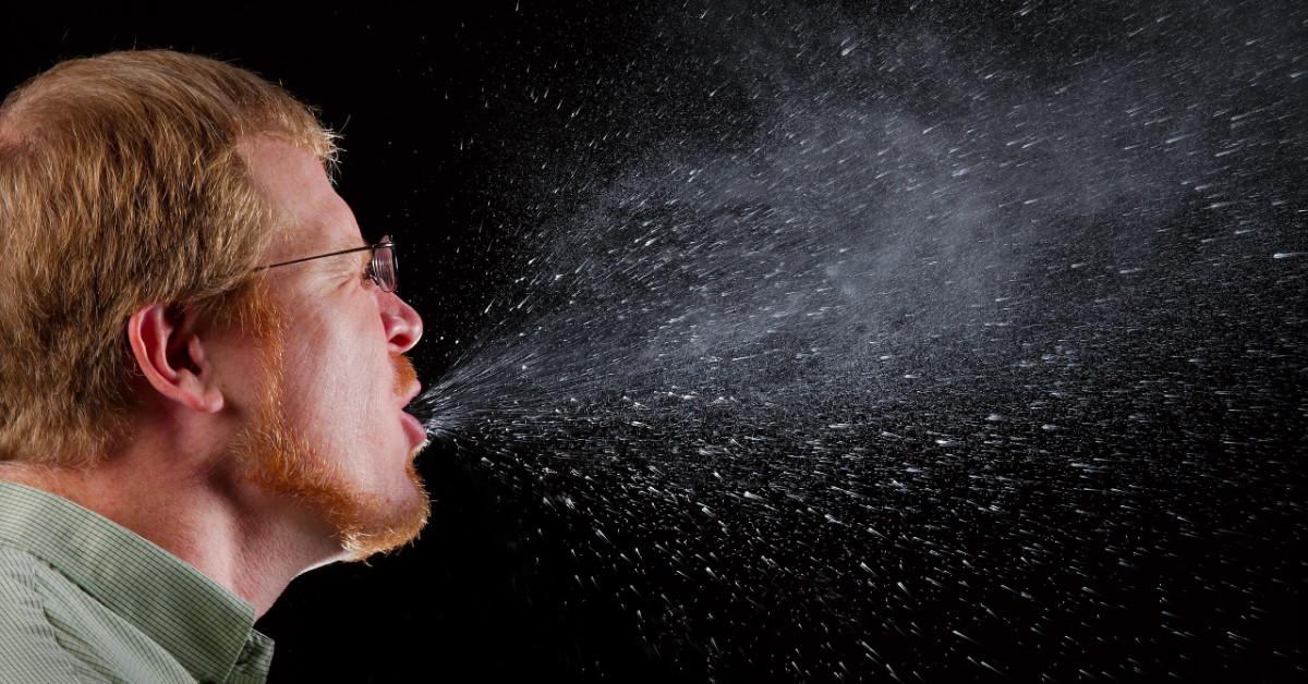 Mann niest und sprüht Speichel in die Luft