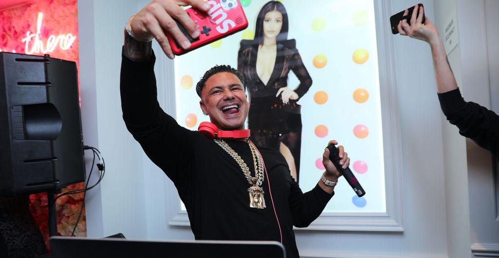 DJ Pauly D usando uma corrente e tirando uma selfie enquanto discoteca com a foto de Kylie Jenner atrás dele