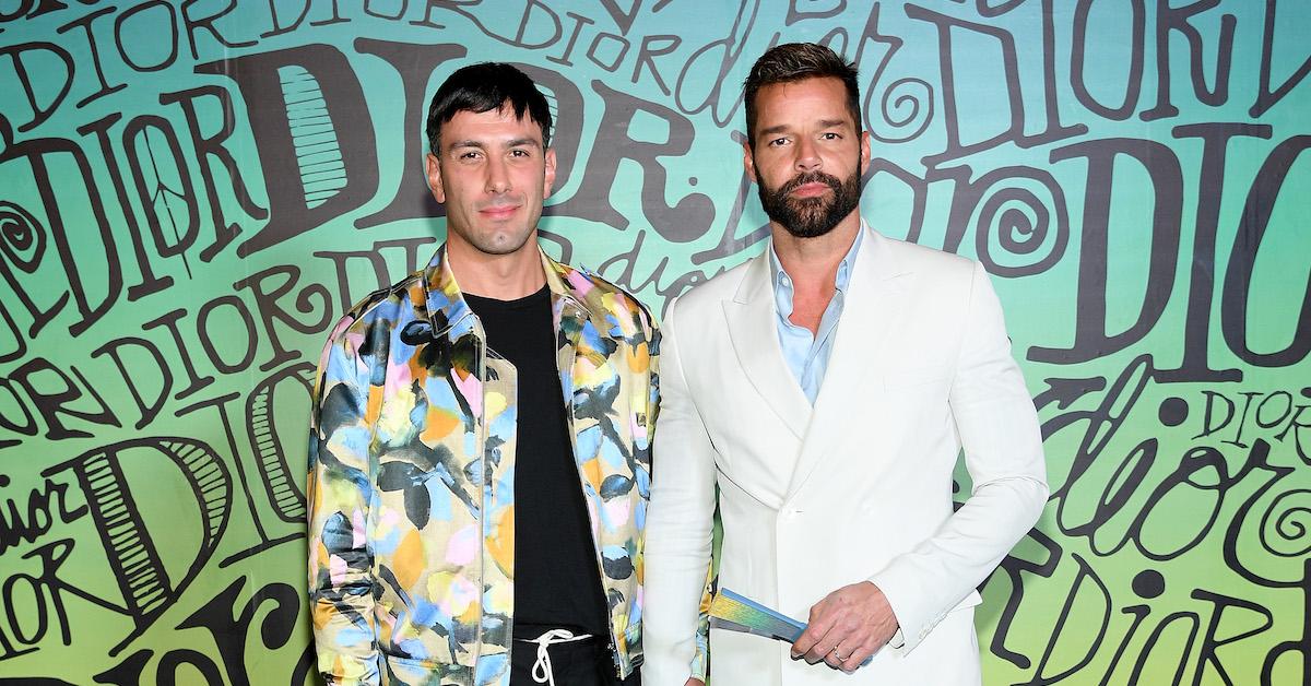 Ricky Martin iført hvid jakke og Jwan Yosef iført farverig jakke foran Dior-væggen