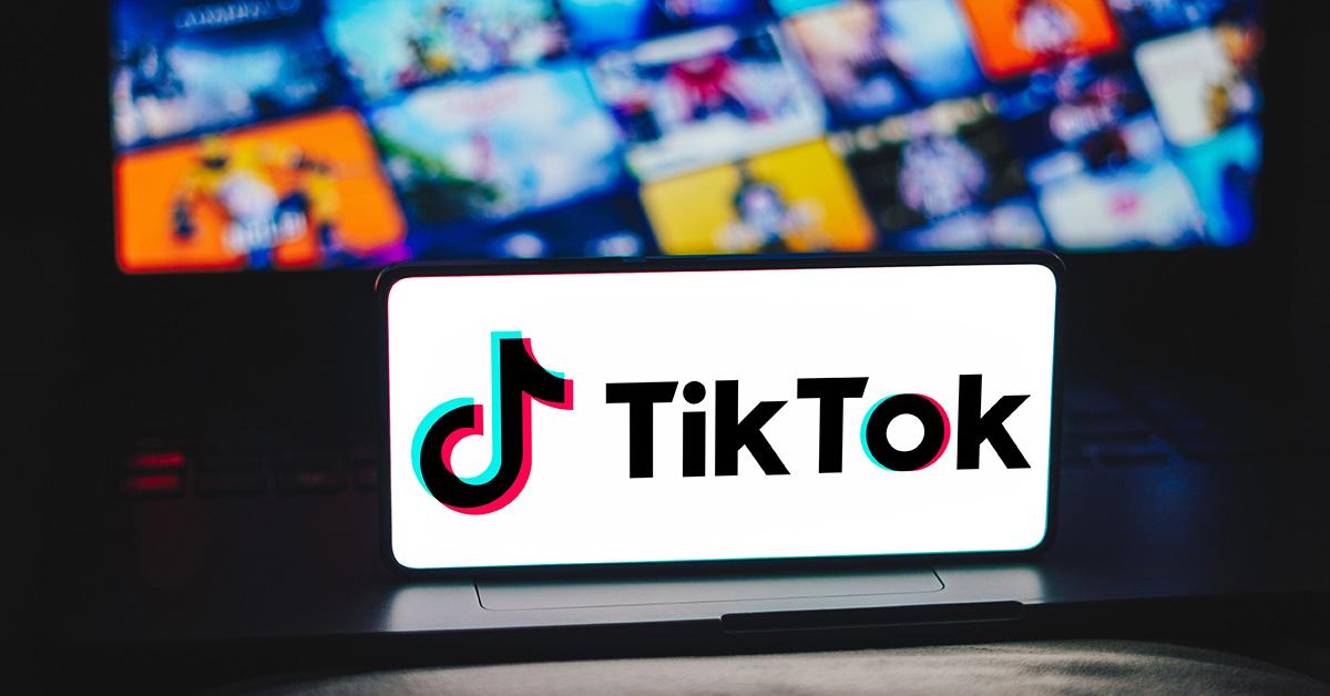 Um logotipo do TikTok na tela de um telefone com um laptop atrás dele. 