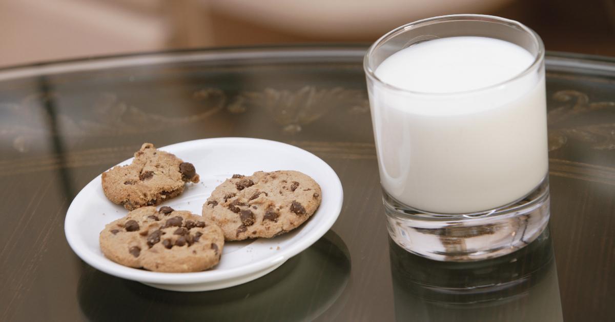Un piatto di biscotti con gocce di cioccolato insieme ad un bicchiere di latte.